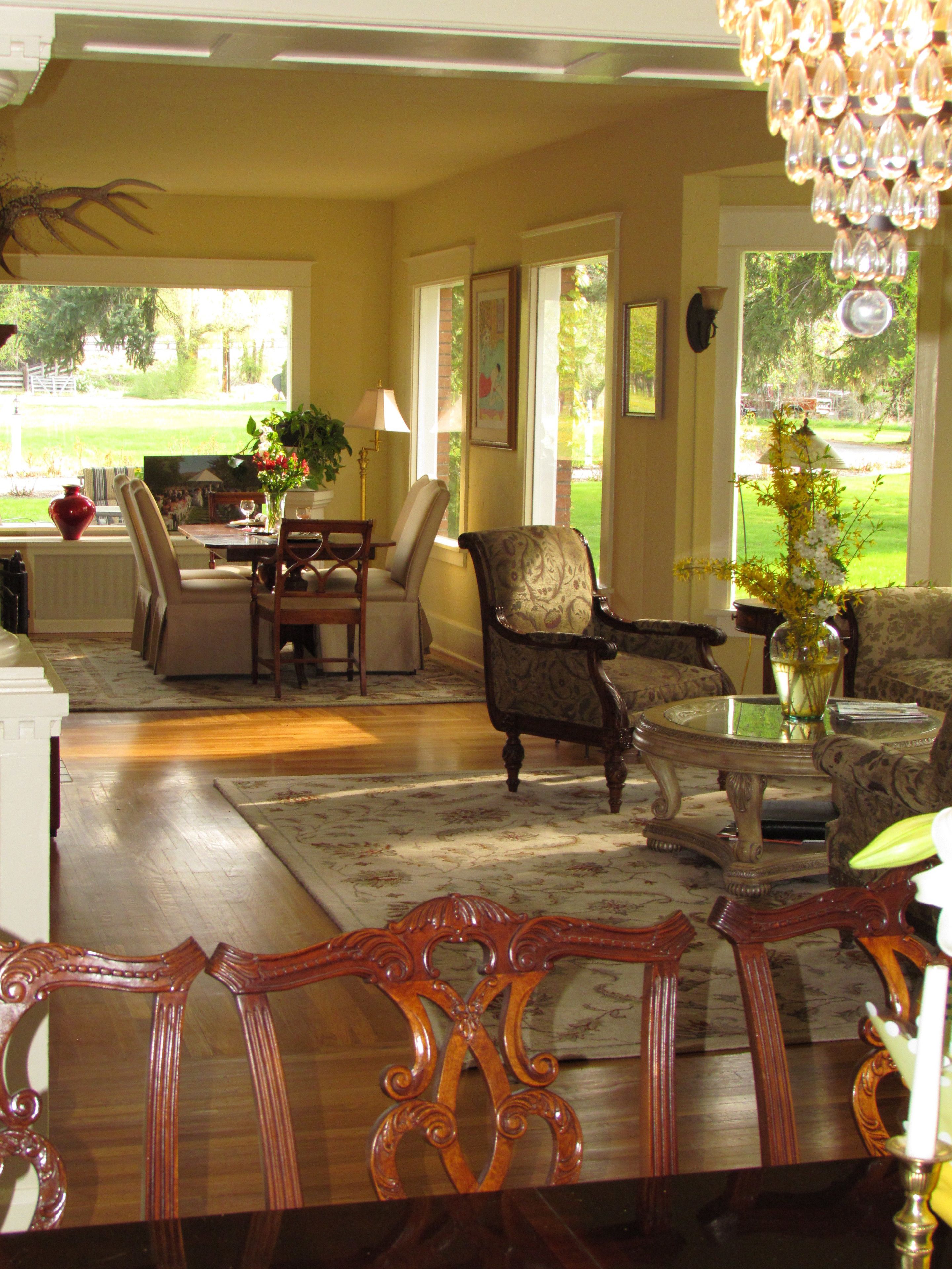 A spacious living room with a large window, a dining area, and a chandelier.