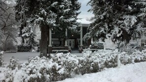A snow-covered house with a front porch, steps leading to the entrance, and a driveway.