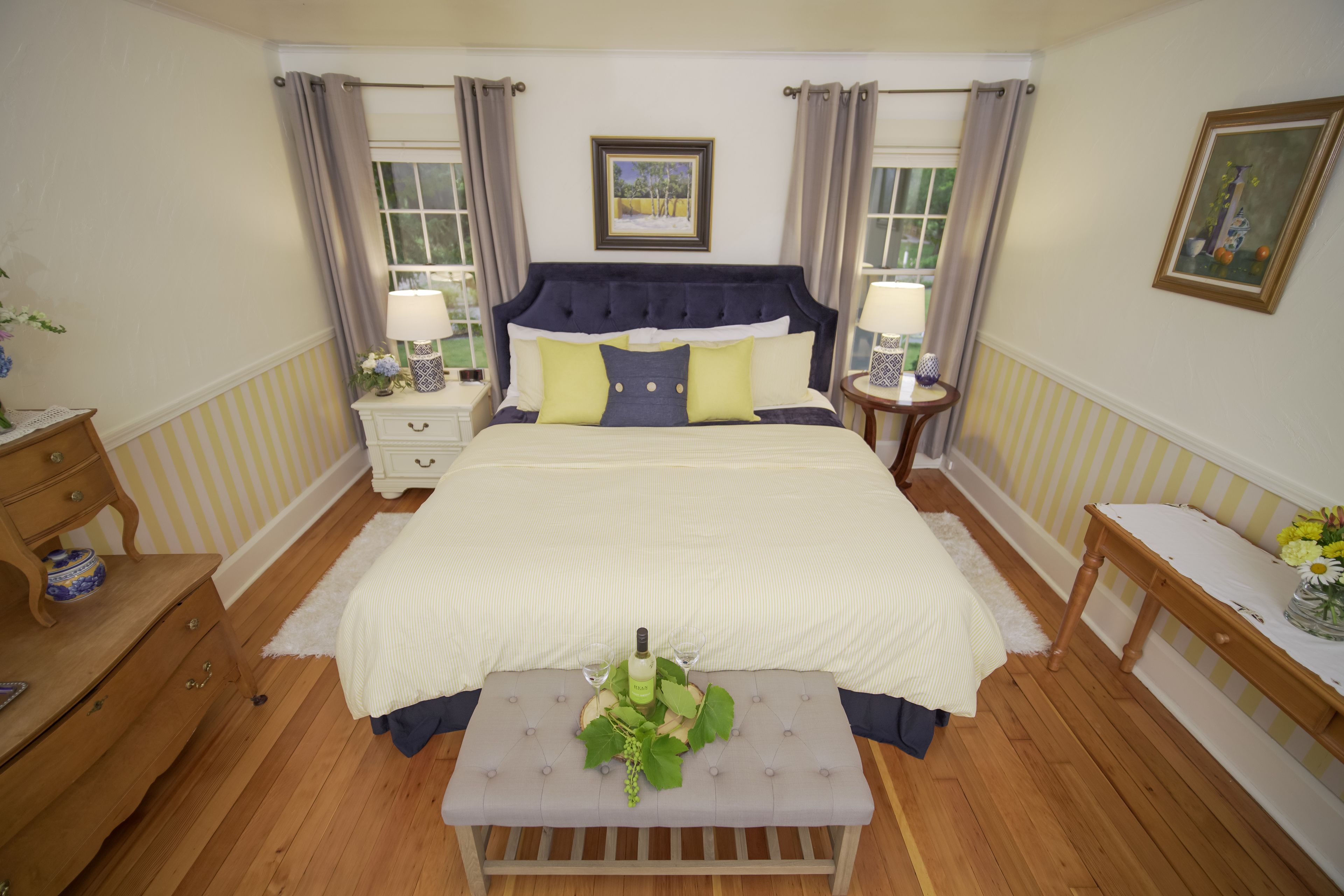 A bedroom with a large bed, two bedside tables, a bench, and a window with curtains.