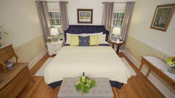 A bedroom with a large bed, two bedside tables, a bench, and a window with curtains.