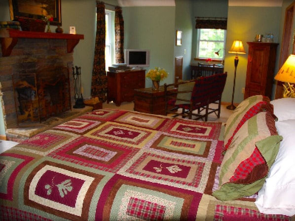 Una habitación acogedora con una cama grande, una chimenea, un escritorio con computadora y una silla.