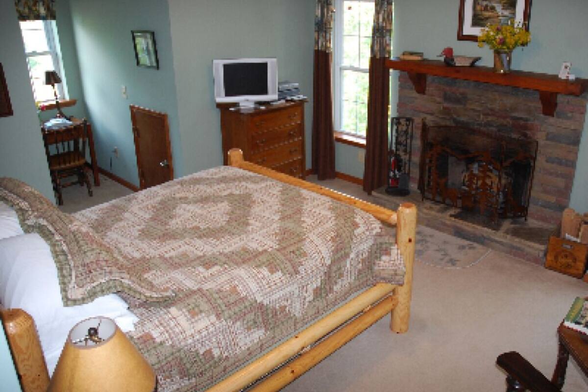 A bedroom with a bed, a television, a fireplace, and a desk with a chair.