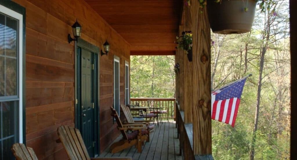 A wooden cabin with a porch, two rocking chairs, and an American flag.