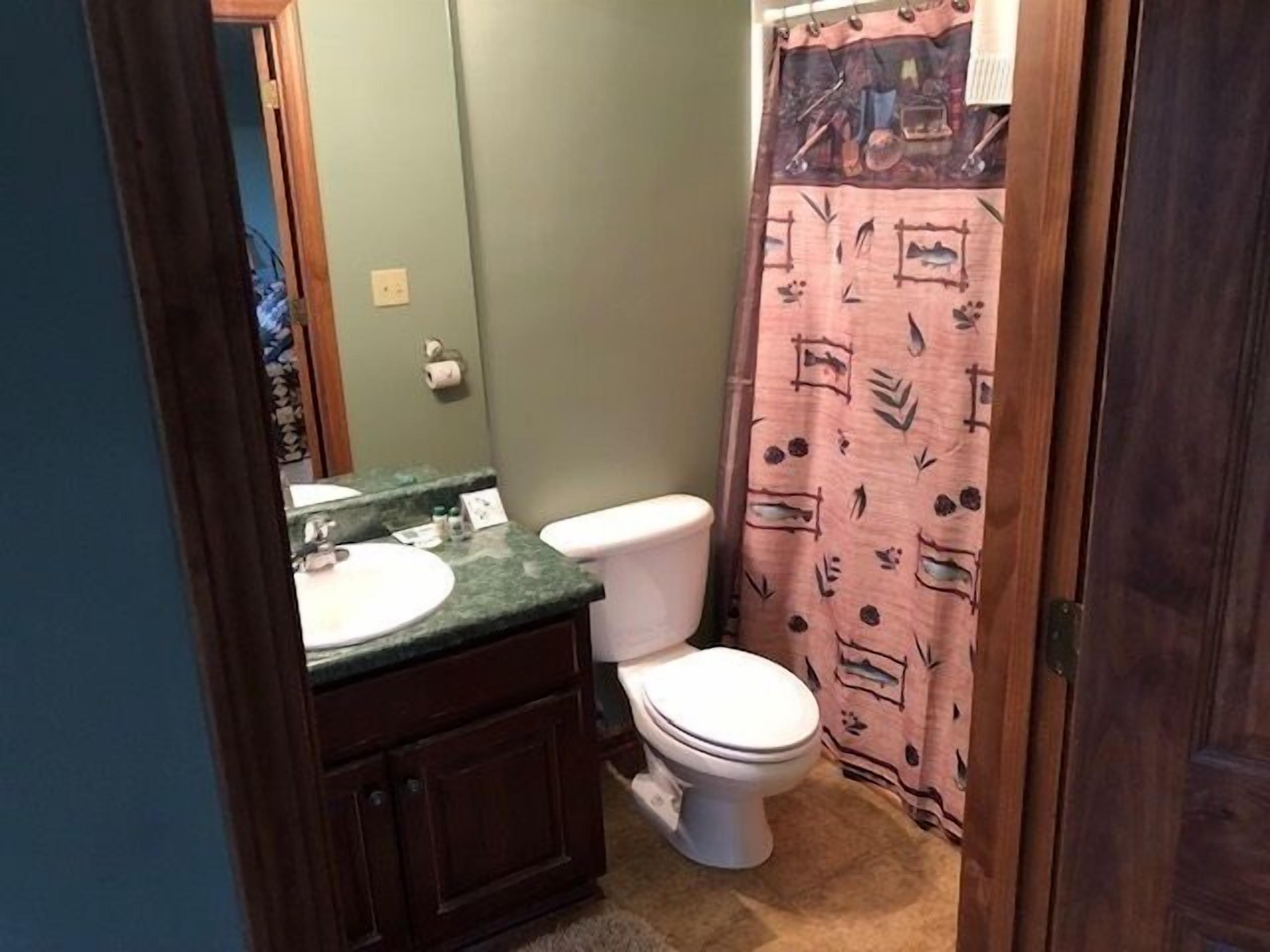 Un baño con inodoro blanco, lavamanos y cortina de ducha estampada.