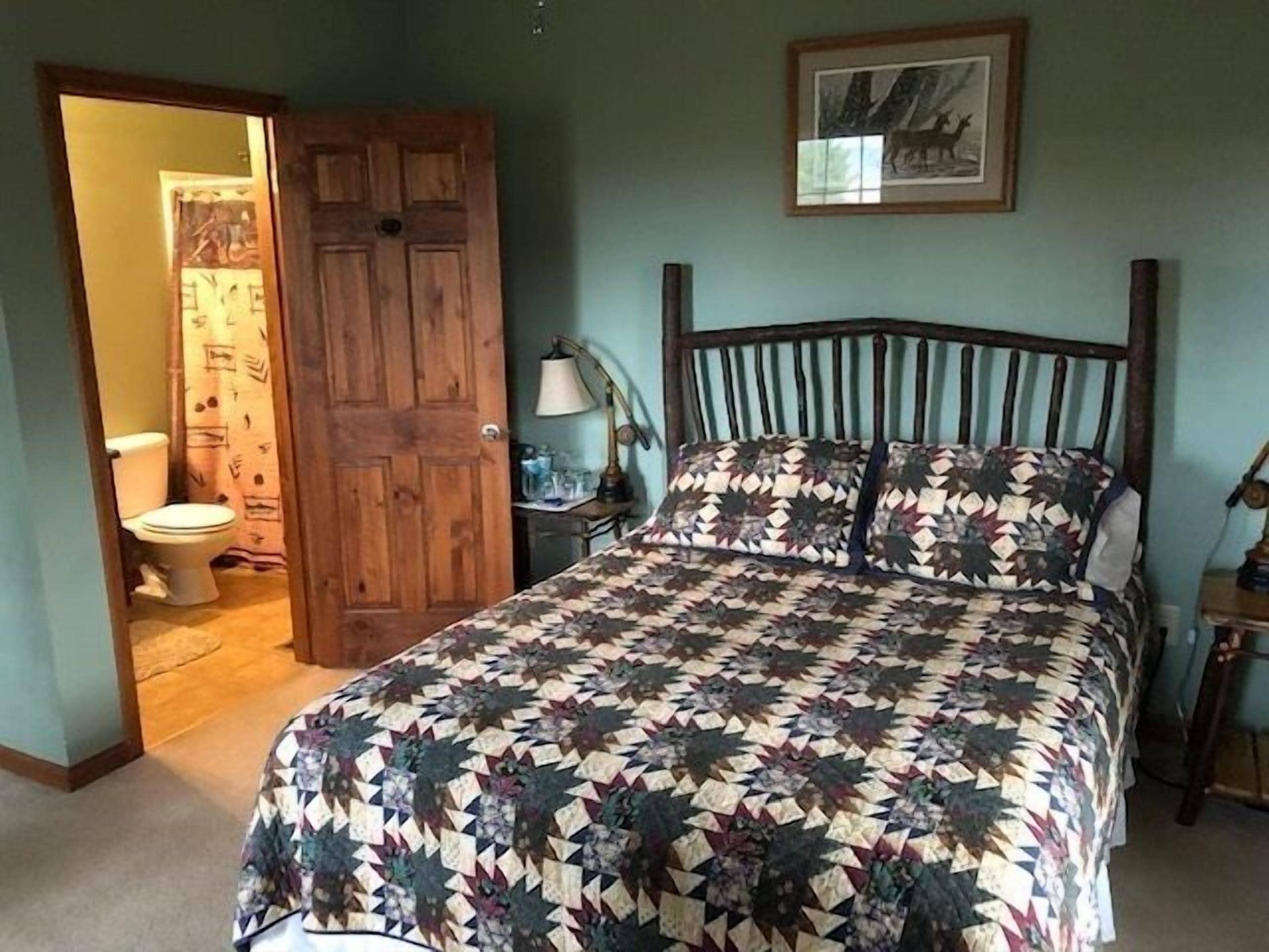 Een slaapkamer met een houten bed, een bed met een patroon, een nachtkastje met een lamp en een lijst op de muur.