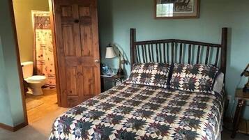 Een slaapkamer met een houten bed, een bed met een patroon, een nachtkastje met een lamp en een lijst op de muur.