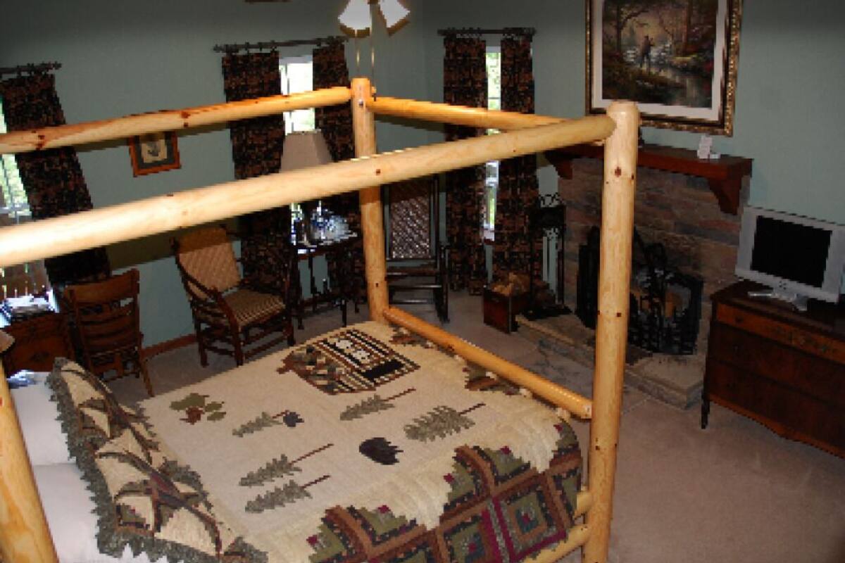 A room with a wooden bed frame, a patterned rug, a television, and a fireplace.