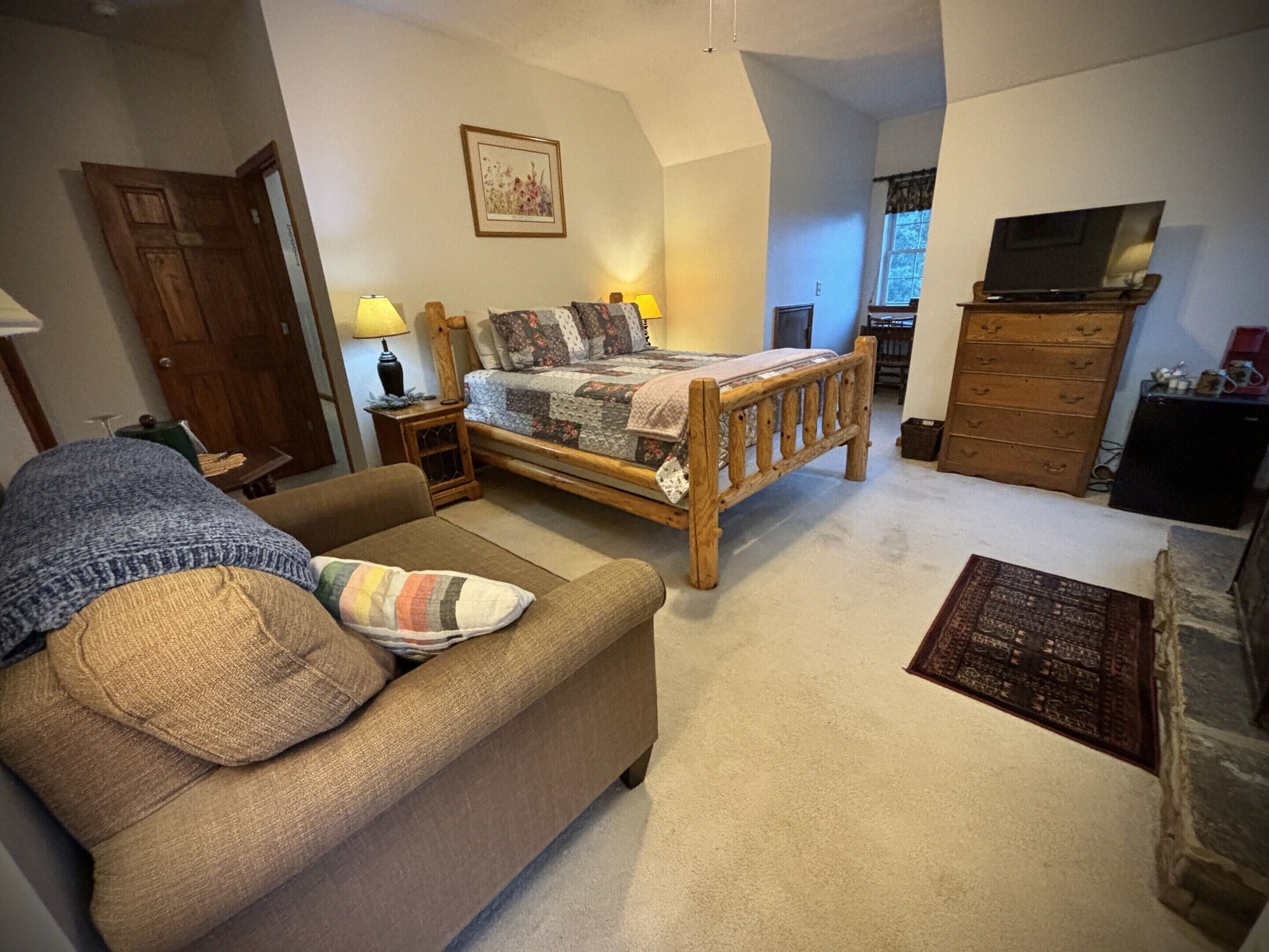 A bedroom with a wooden bed, a wooden dresser, a television, and a sofa.