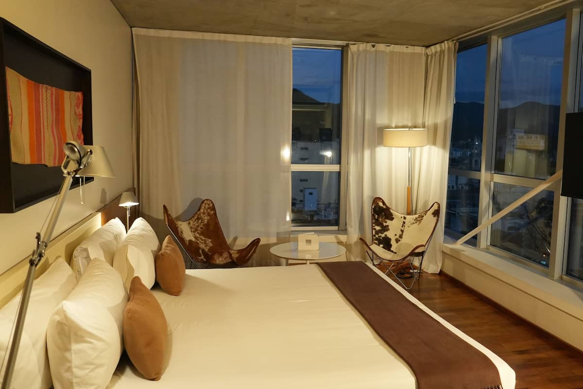 A hotel room with a large bed, two chairs, a small table, and a TV.