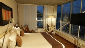 A hotel room with a large bed, two chairs, a small table, and a TV.