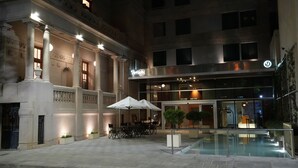 A courtyard with a pool, outdoor seating, and a building with columns and a modern entrance.