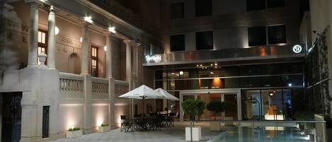 A courtyard with a pool, outdoor seating, and a building with columns and a modern entrance.