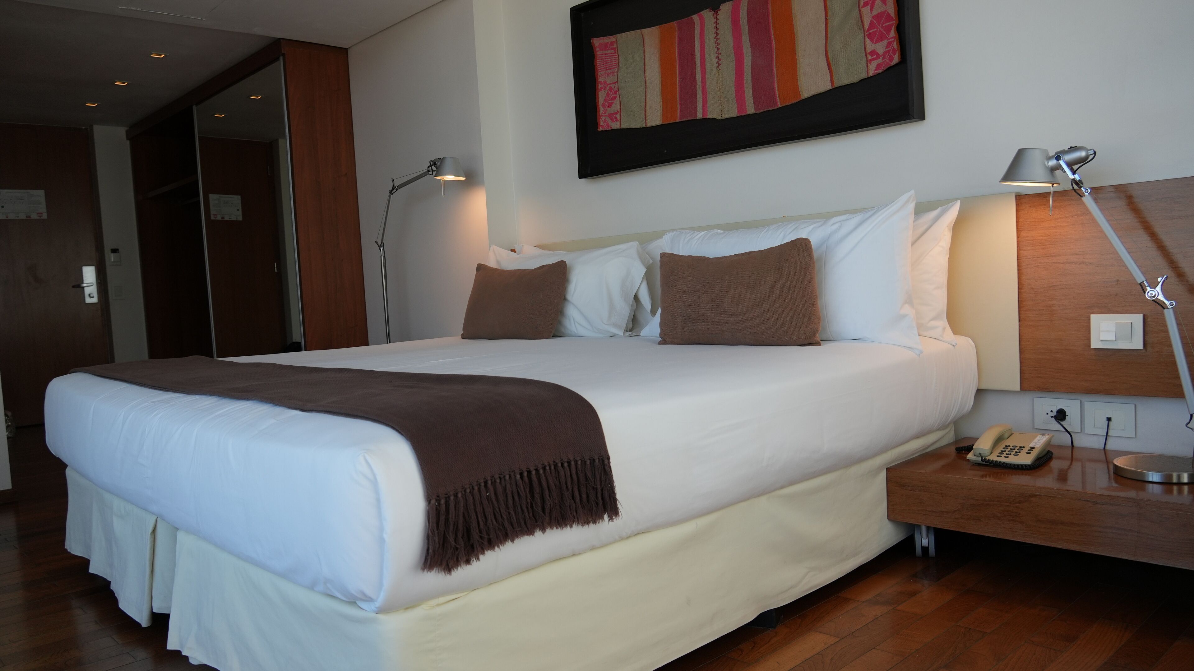 Ein Hotelzimmer mit einem großen Bett, zwei Nachttischlampen, einem Telefon und einem Gemälde an der Wand.