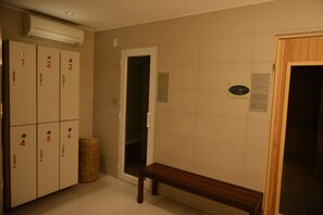 A hotel room with numbered lockers, a bench, a trash bin, and a door leading to another room. - Design Suites Salta (Salta)