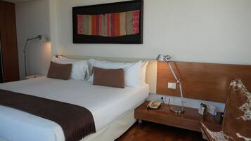 A neatly made bed with white and brown bedding, a wooden headboard, a bedside table with a lamp, a phone, and a small nightstand.