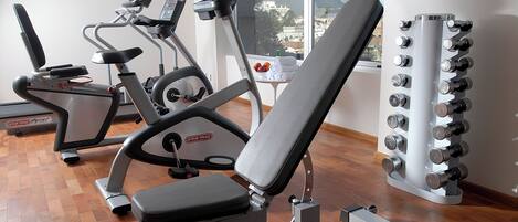 Ein Fitnessstudio mit Trainingsgeräten, darunter eine Bank, ein Laufband und ein Gewichte-Turm.