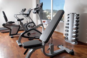 Una palestra con attrezzature per esercizi, tra cui una panca, un tapis roulant e una batteria di pesi.