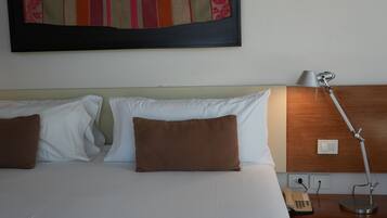 Een hotelkamer met een bed, twee kussens, een bedlampje, een telefoon en een lichtschakelaar aan de muur.