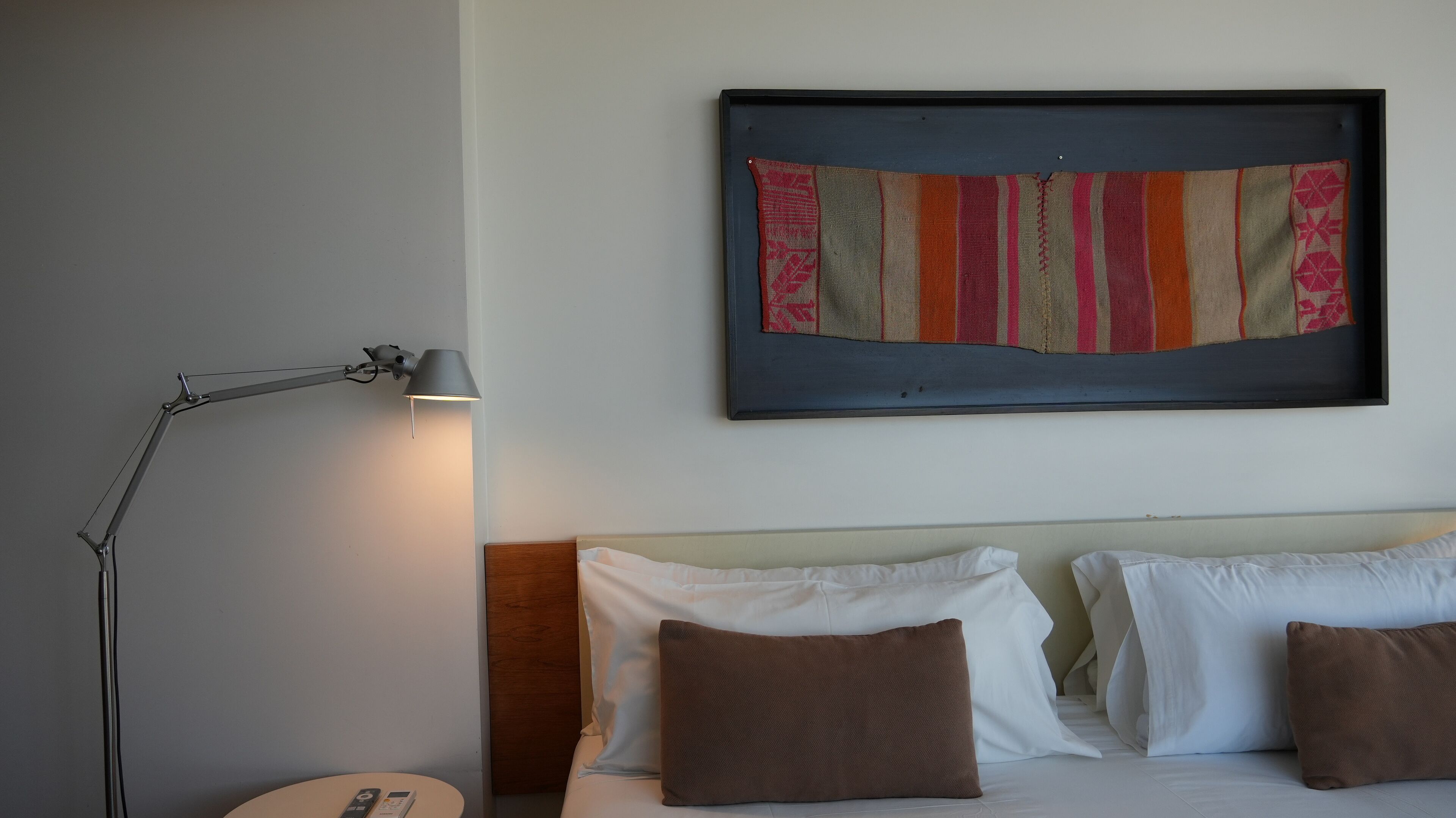 A hotel room with a bed, pillows, a bedside table, a lamp, and a framed artwork on the wall.