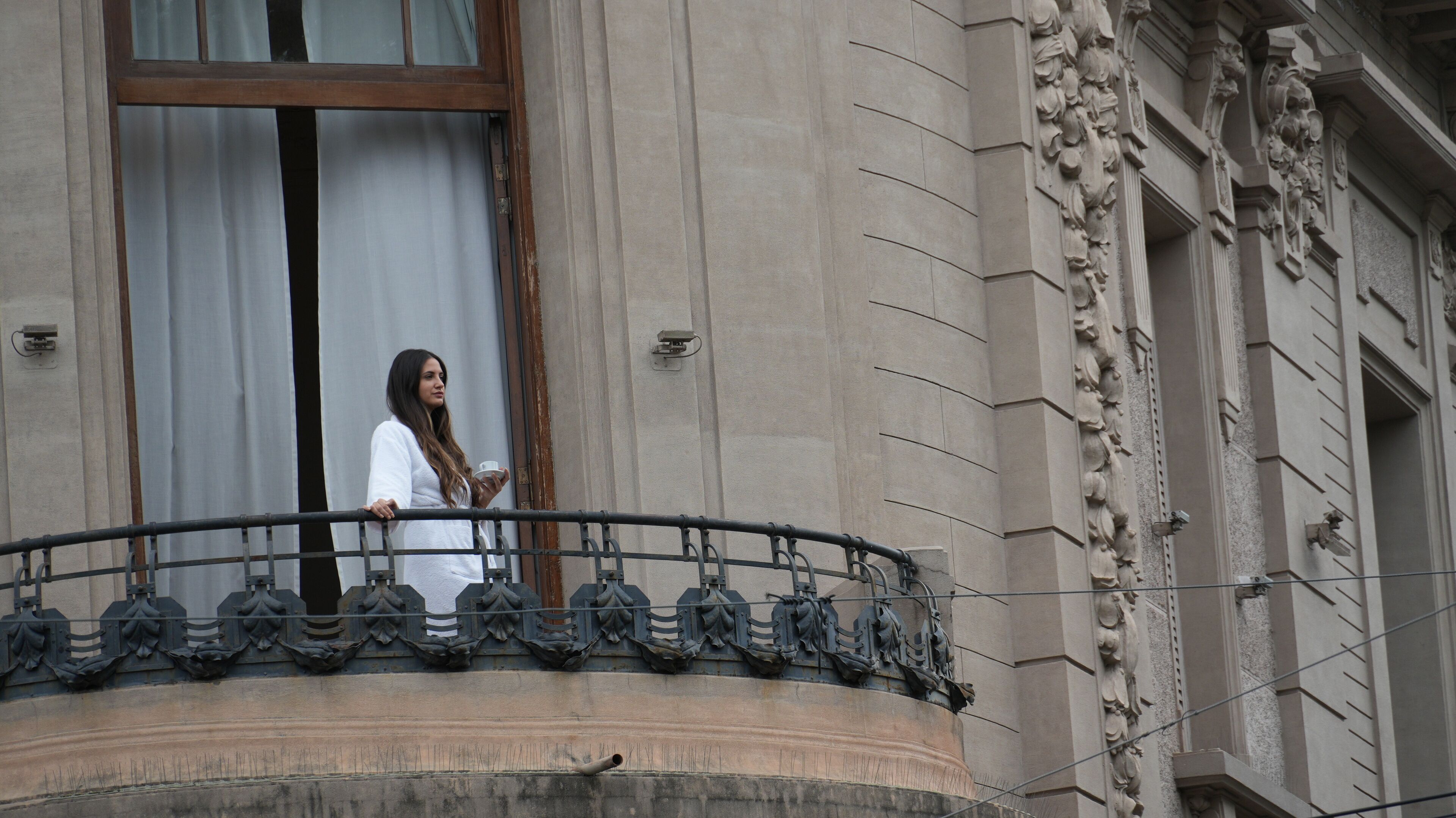 A balcony with ornate metal railings and a building facade with classical architectural details.