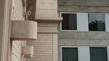 Une façade d’immeuble de couleur beige, avec une partie en béton et trois fenêtres dotées de rideaux.