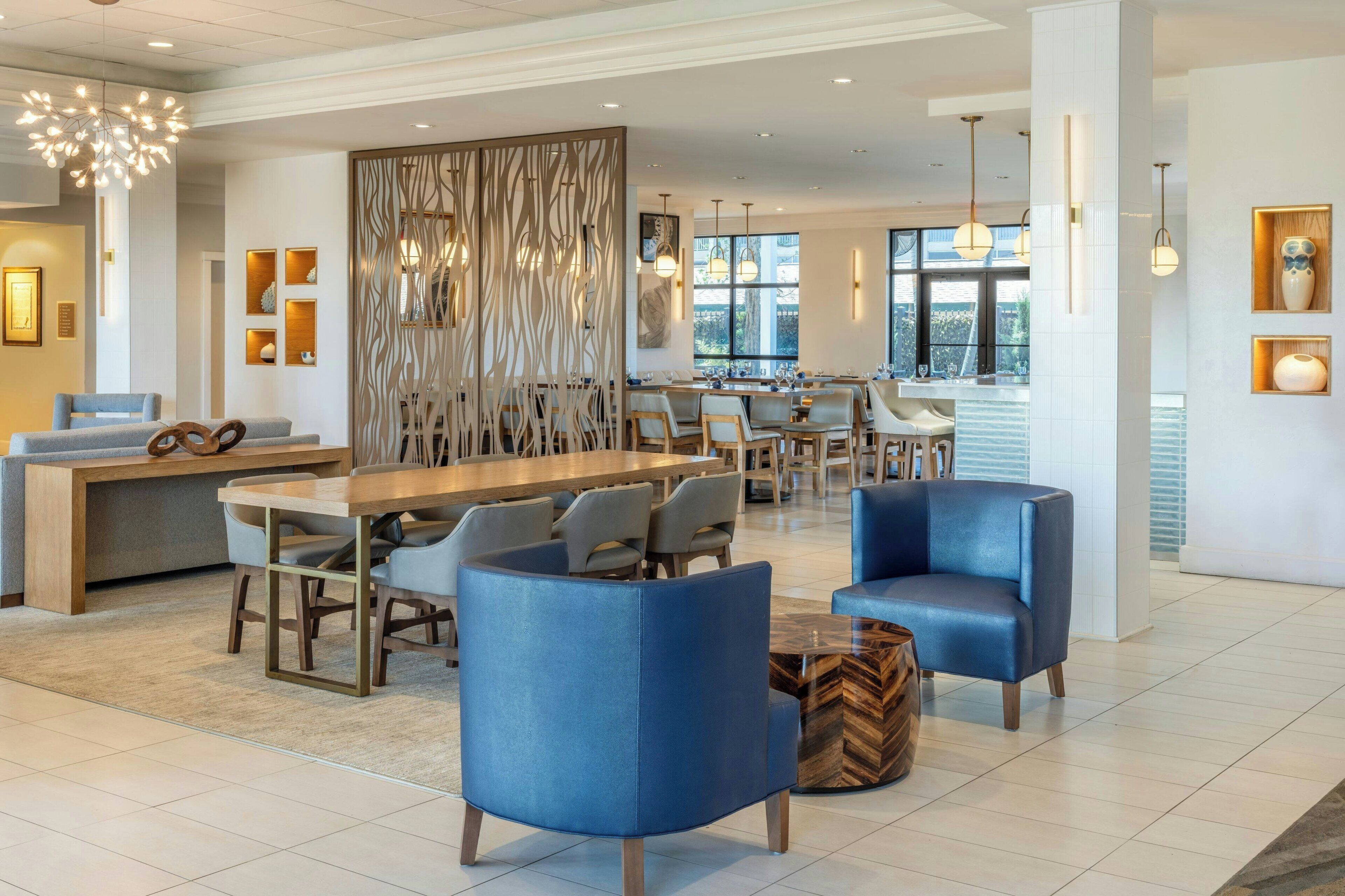 A modern hotel lobby with a long reception desk, blue armchairs, and a decorative wall.