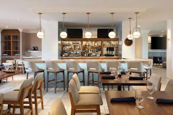 A modern bar area with a wine rack, bar stools, and a counter with a variety of bottles. - Four Points by Sheraton Punta Gorda Harborside (Punta Gorda)