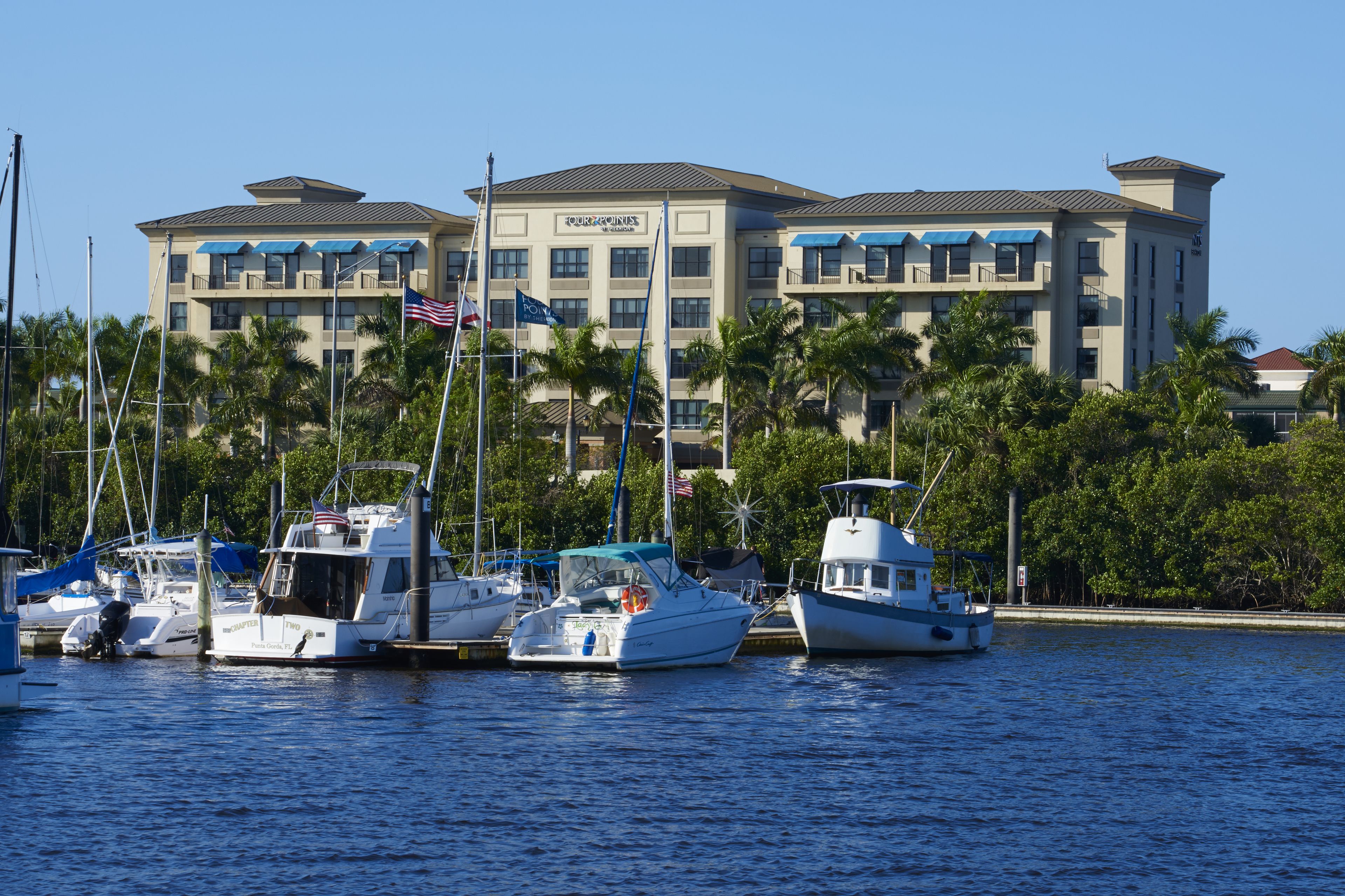 A marina with several boats docked in front of a hotel with multiple balconies and flags.