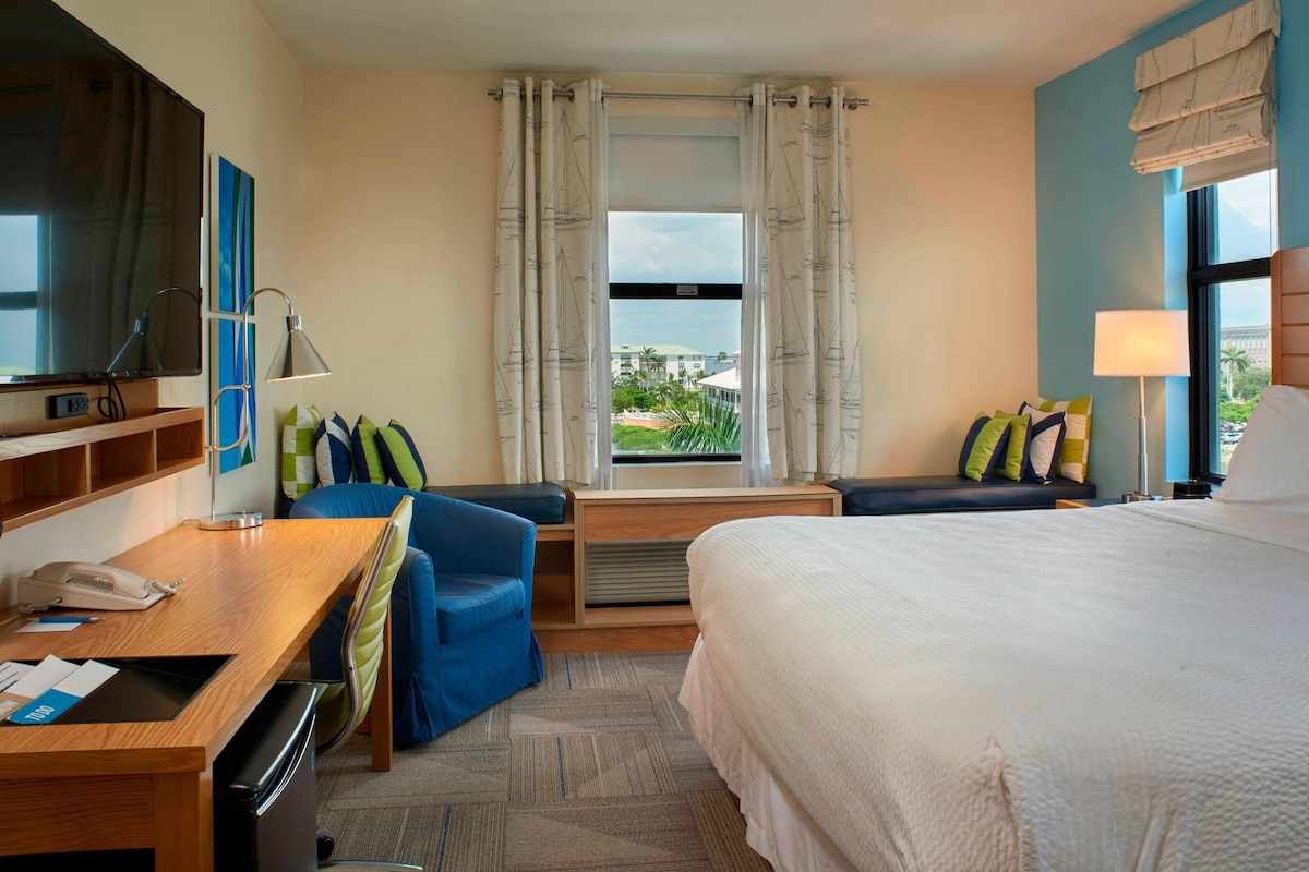 A hotel room with a bed, desk, chair, and a view of the outdoors.