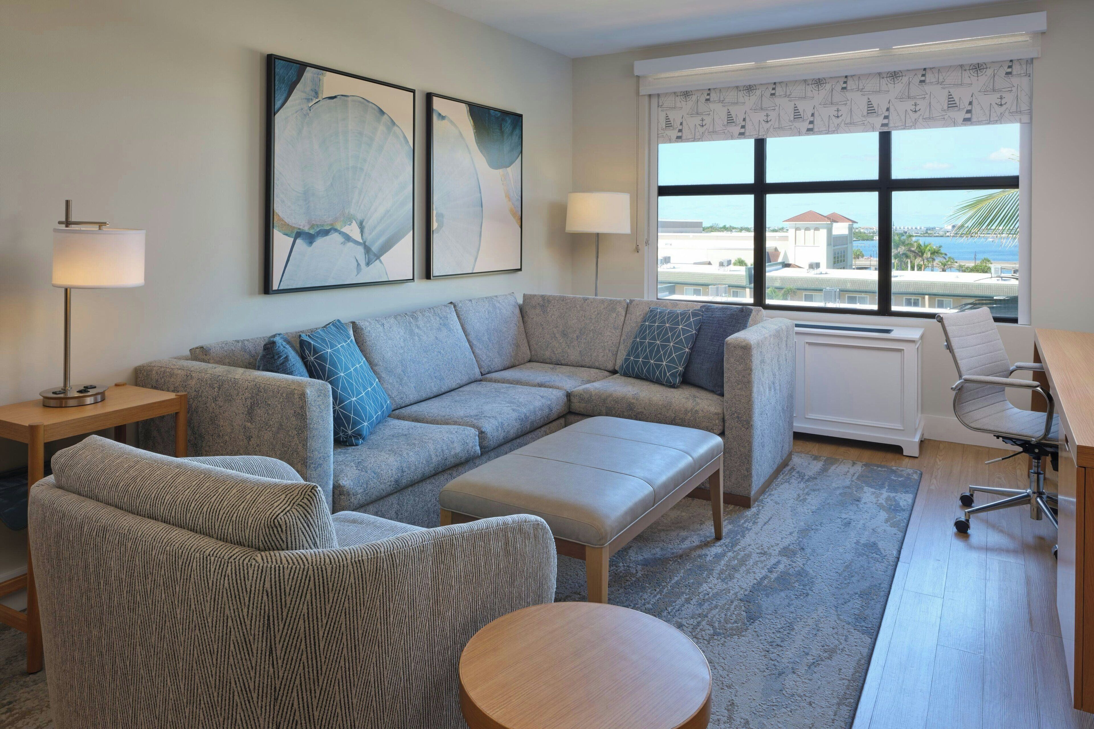 A modern living room with a sectional sofa, a round coffee table, and a view of the ocean through large windows.