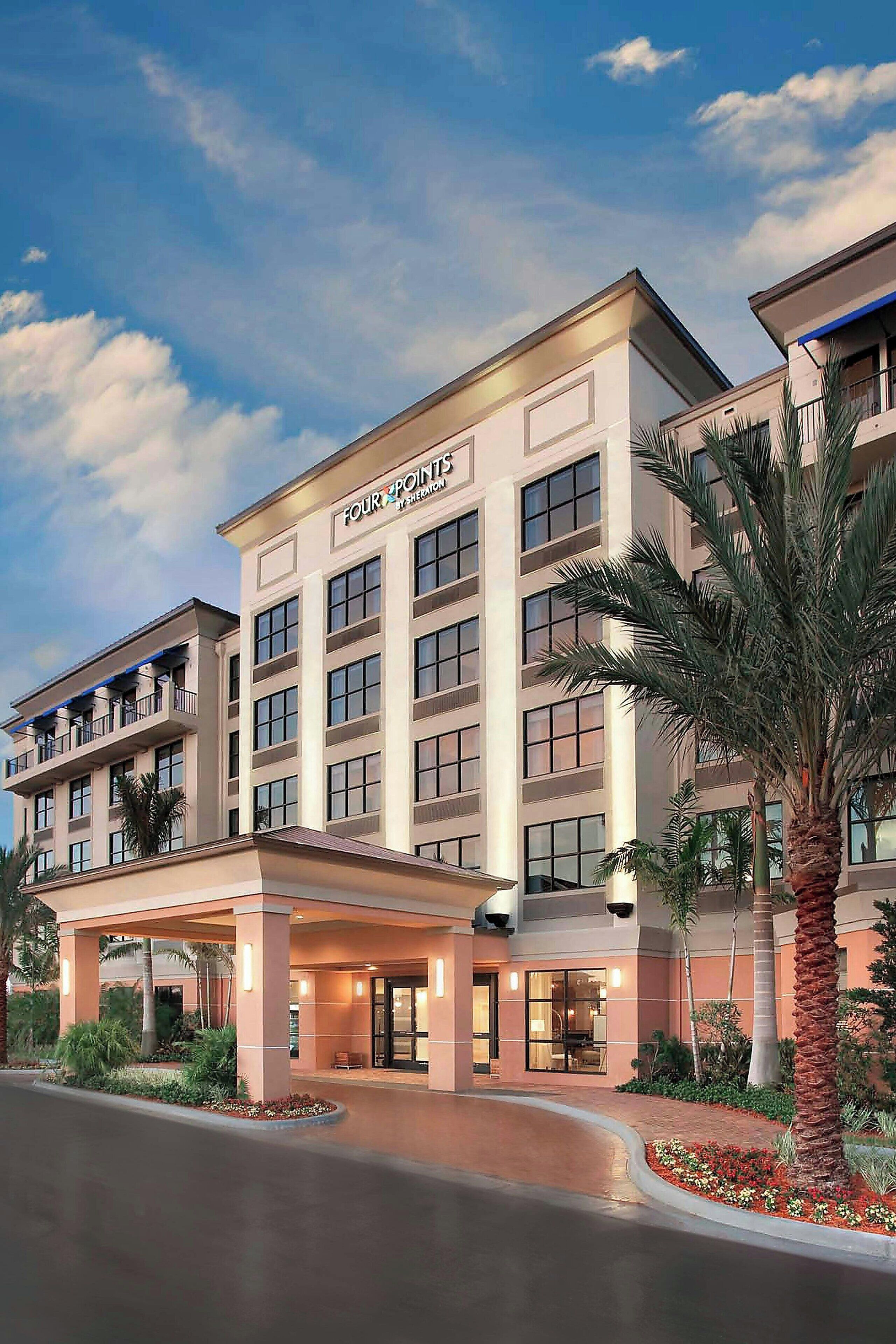 A multi-story hotel with a prominent entrance, large windows, and a landscaped area with palm trees.