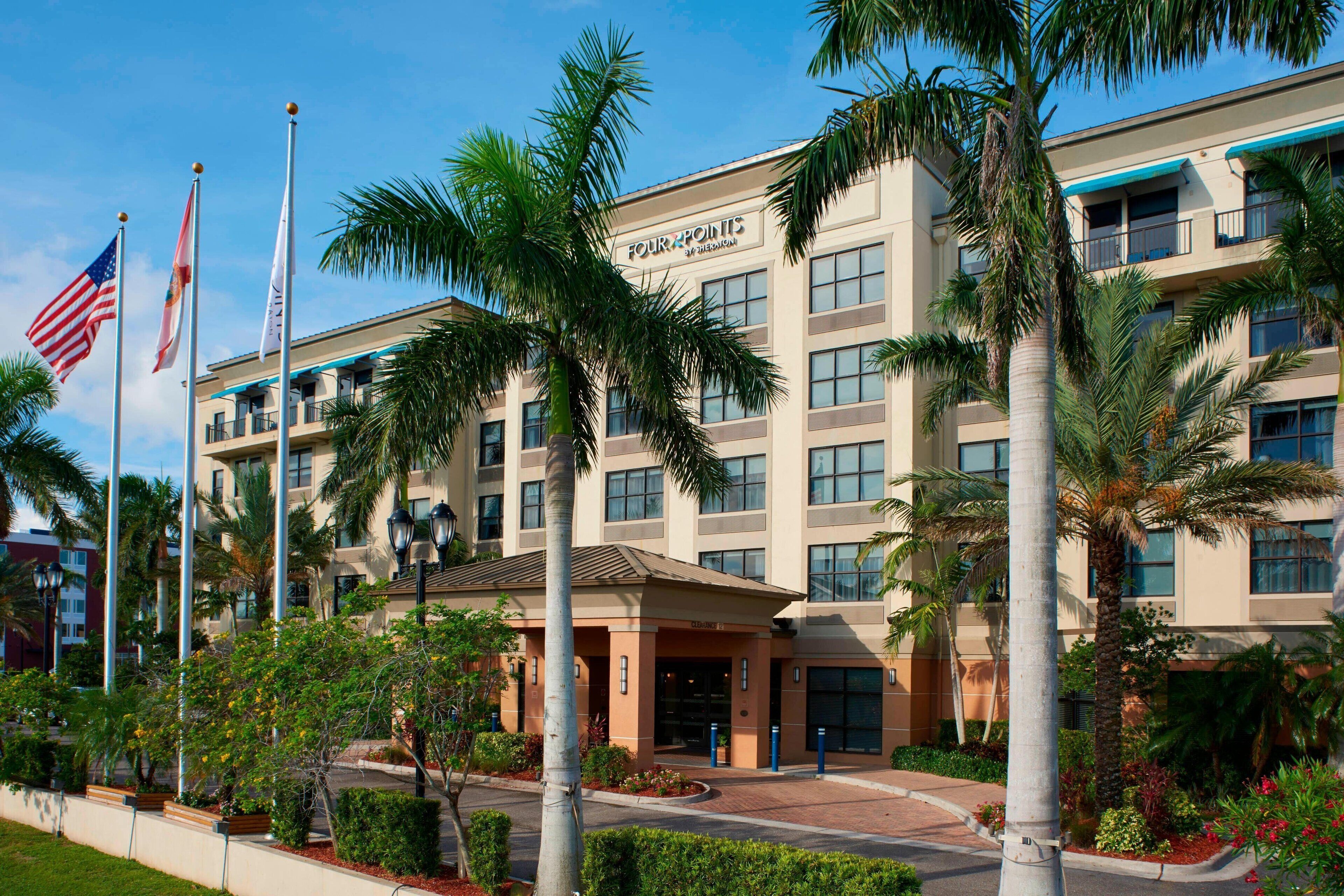 A multi-story hotel with a modern design, featuring a prominent entrance with a covered area and a landscaped garden with palm trees.