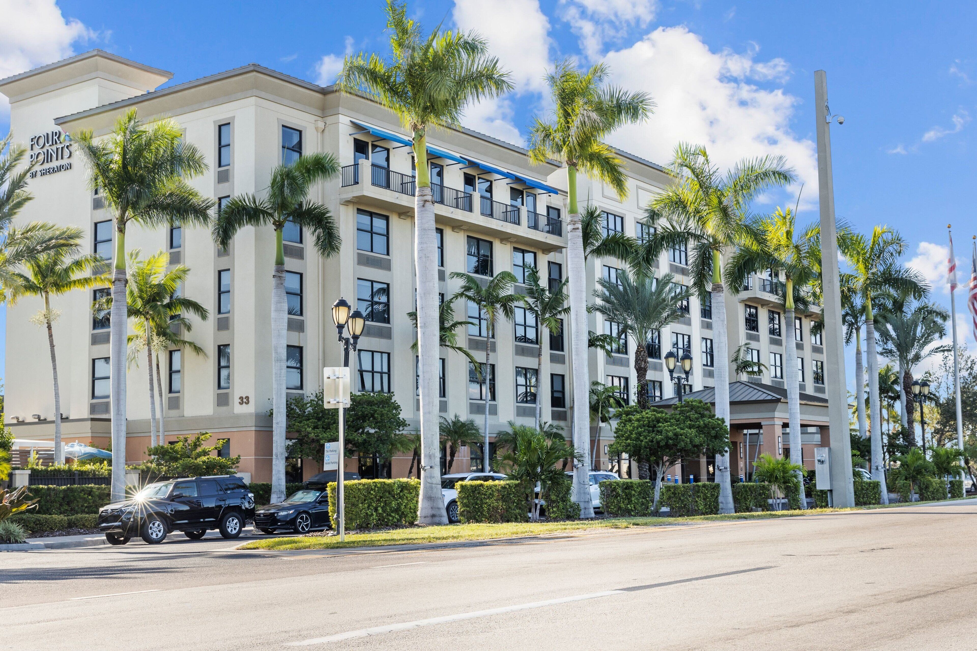 A multi-story hotel with a modern facade, palm trees, and a clear blue sky.