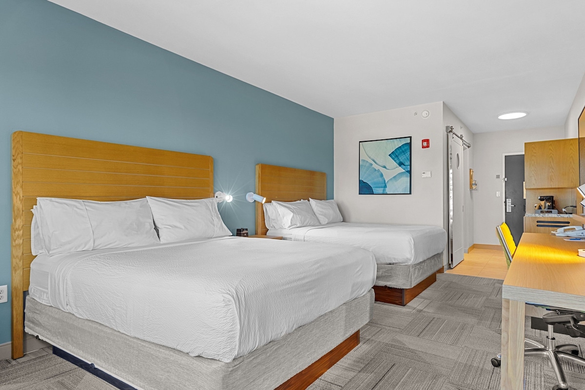 A hotel room with two beds, a desk, and a bathroom.