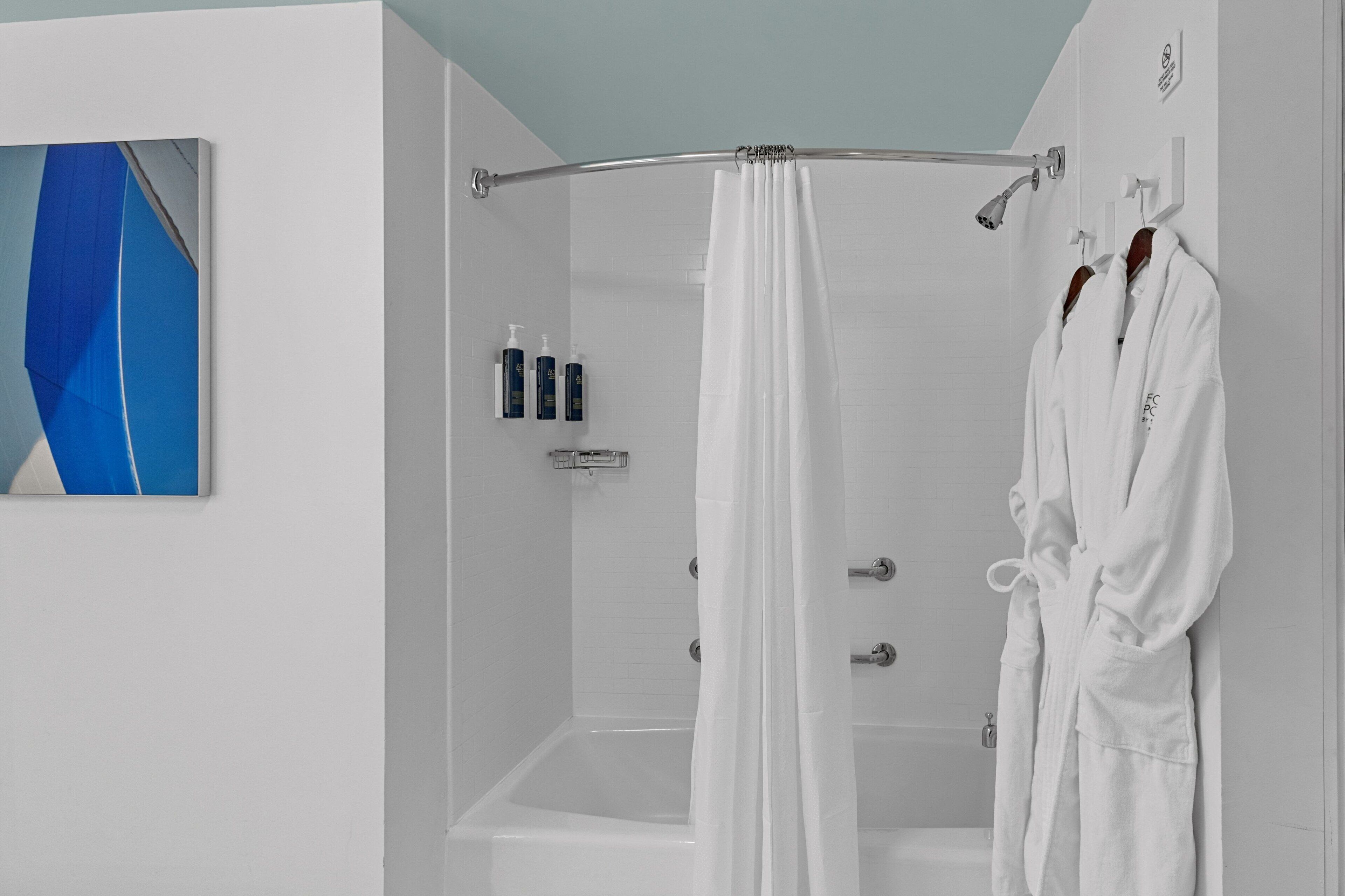 A modern bathroom with a shower, a bathtub, and a towel rack with two white bathrobes.