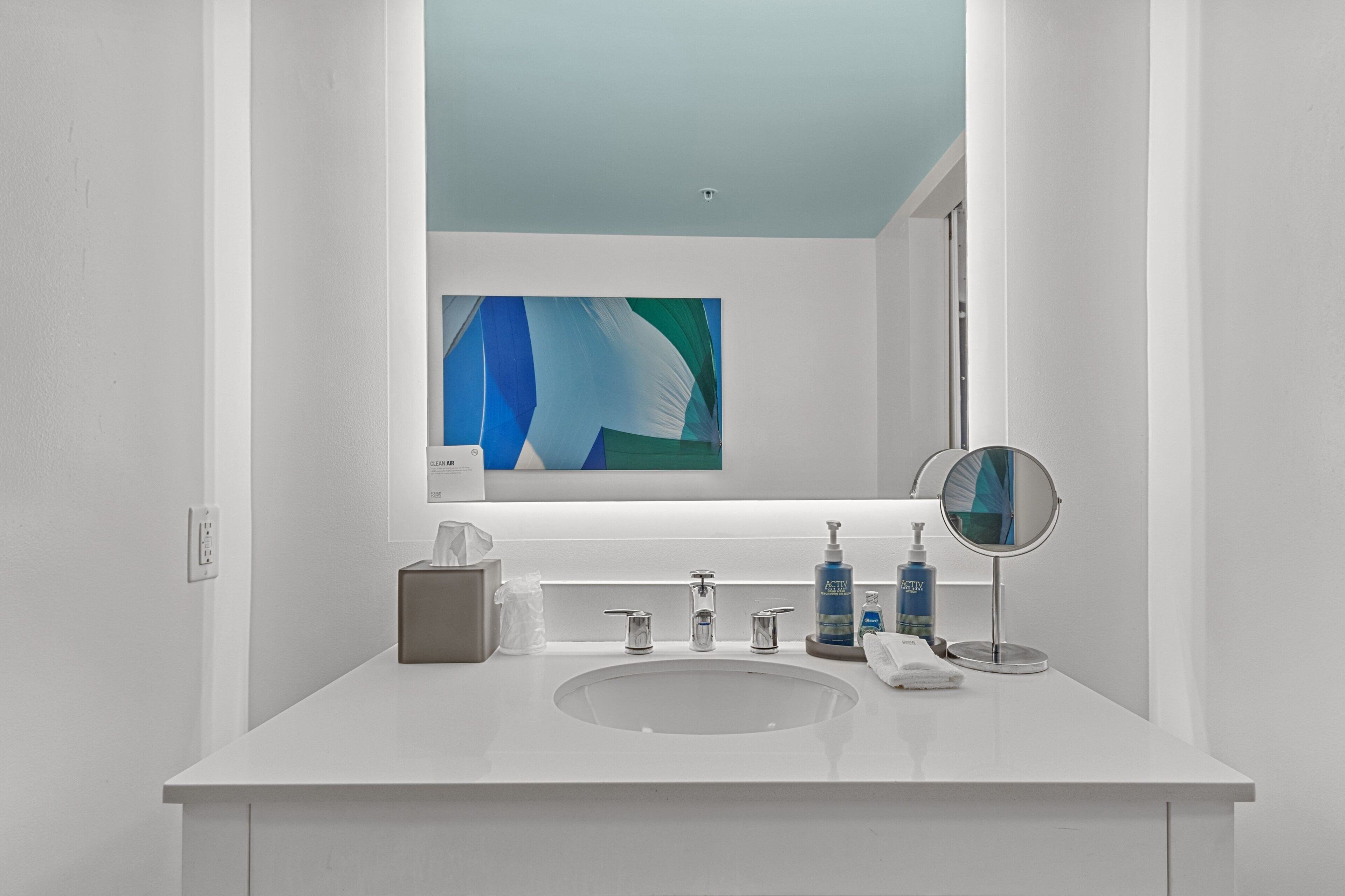 Un baño moderno con un tocador blanco, un espejo redondo y una botella azul de jabón para manos.