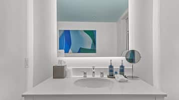 Un baño moderno con un tocador blanco, un espejo redondo y una botella azul de jabón para manos.