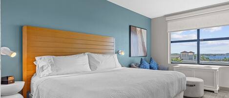 Une chambre d’hôtel moderne avec un grand lit, une vue sur la mer et une fenêtre donnant sur un immeuble.