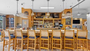 Een bar met houten barstoelen, een goed gevulde drankenkast en hanglampen.