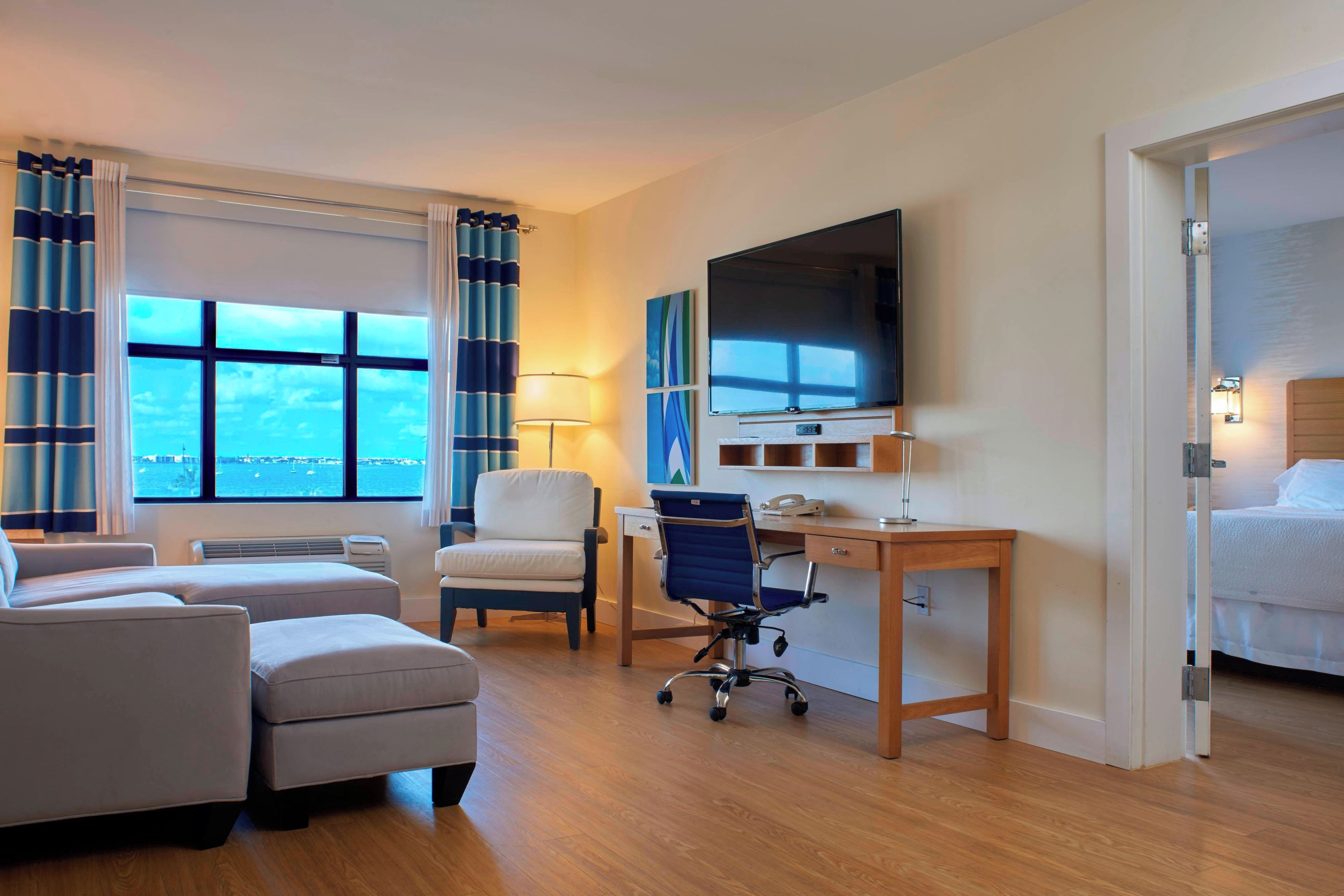 Une chambre d’hôtel avec un lit, un bureau équipé d’un ordinateur, une chaise, un téléviseur et une fenêtre avec des rideaux.