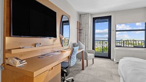 Hotelkamer met een houten bureau, een flatscreen televisie, een stoel, een bed en een balkon met uitzicht.
