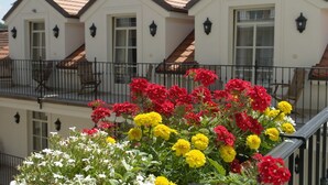 A white building with a tiled roof and multiple windows, surrounded by a balcony with a railing. - Hotel Angelis (Prague)