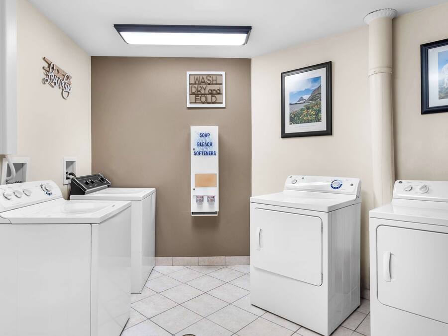 Una lavanderia con due lavatrici e asciugatrici a carica frontale, un dispenser di sapone fissato al muro e un quadro con una veduta di montagna.