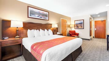 Una habitación de hotel con una cama grande, dos mesitas de noche con lámparas, una silla roja y dos puertas.