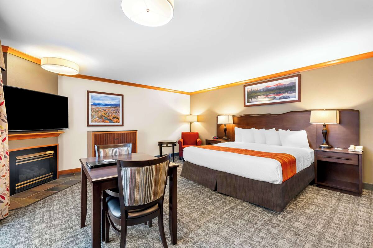 Een hotelkamer met een bed, een bureau met stoel, een televisie, een open haard en twee lampen.