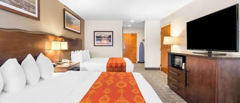 A hotel room with two beds, a TV, a desk with a lamp, and a wardrobe.