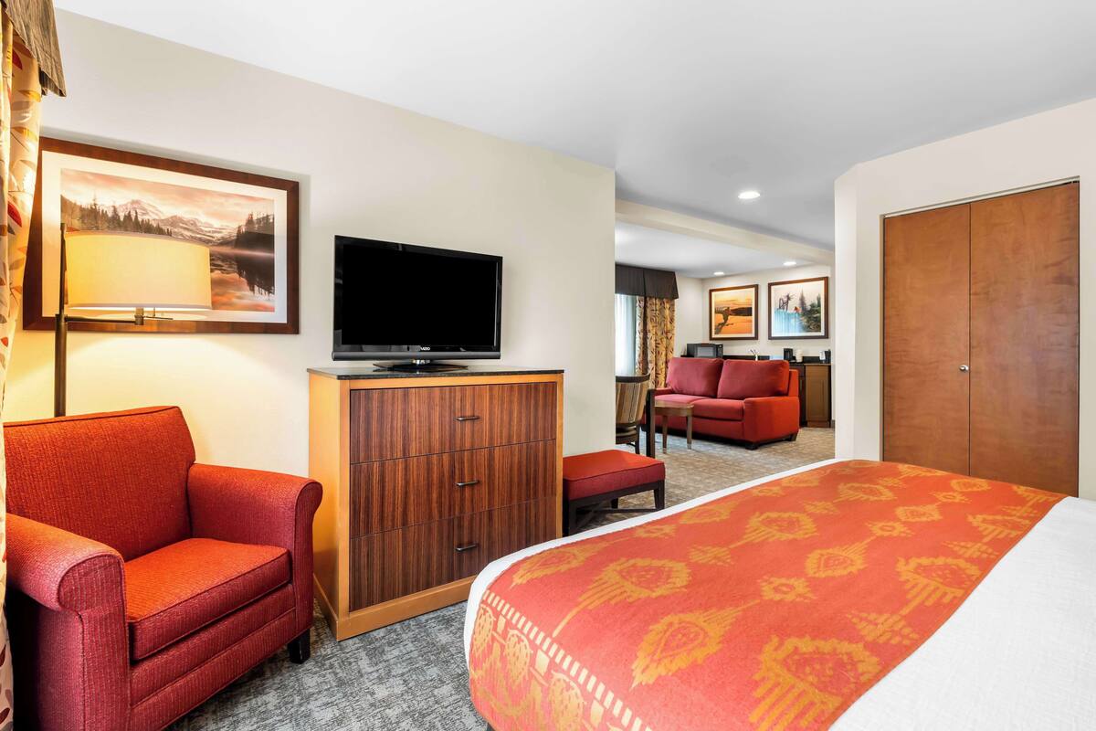Een hotelkamer met een groot bed, een televisie op een houten kast, een rode fauteuil, een rode bank en een houten garderobe.