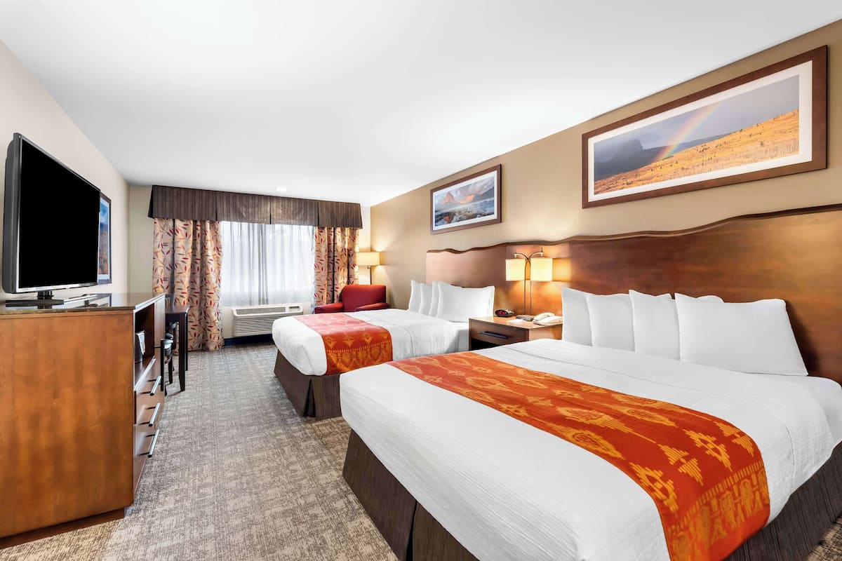 Een hotelkamer met twee bedden, een bureau, een televisie en een groot raam met gordijnen.