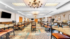 Un comedor de hotel amplio con varias mesas y sillas, un candelabro y un televisor de pantalla plana montado en la pared.