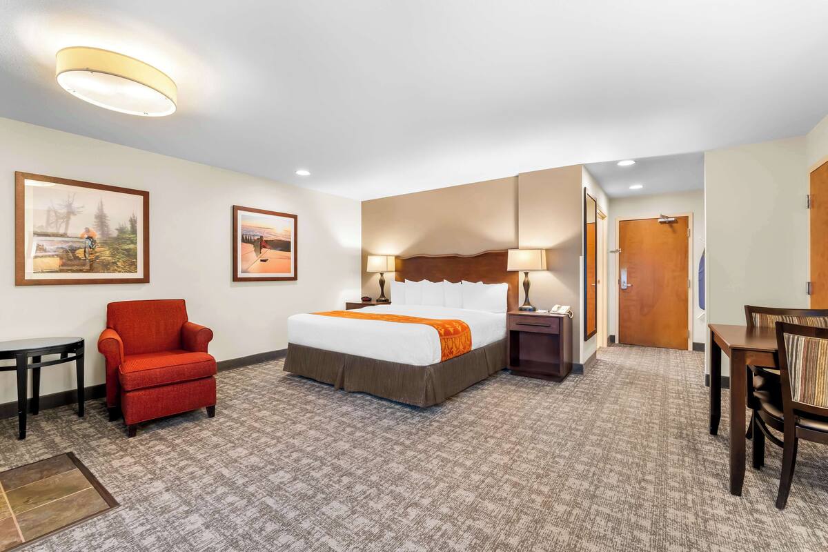 Een hotelkamer met een bed, een rode fauteuil, een houten tafel en een bureau.